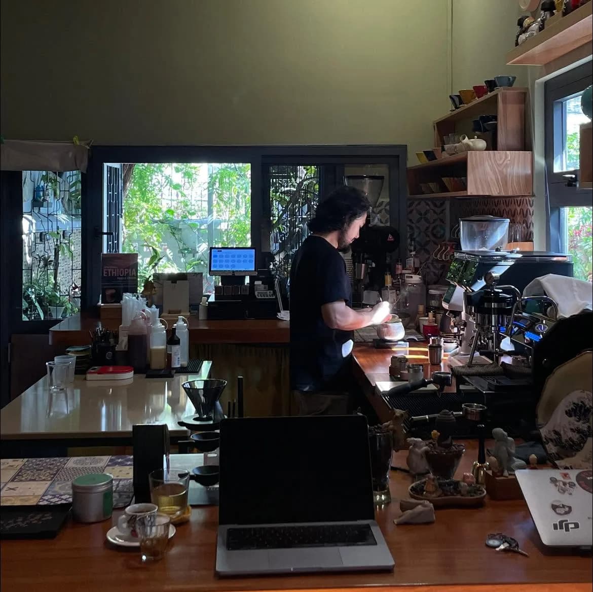 A laptop open beside coffee equipment while Long Huỳnh works in a café.