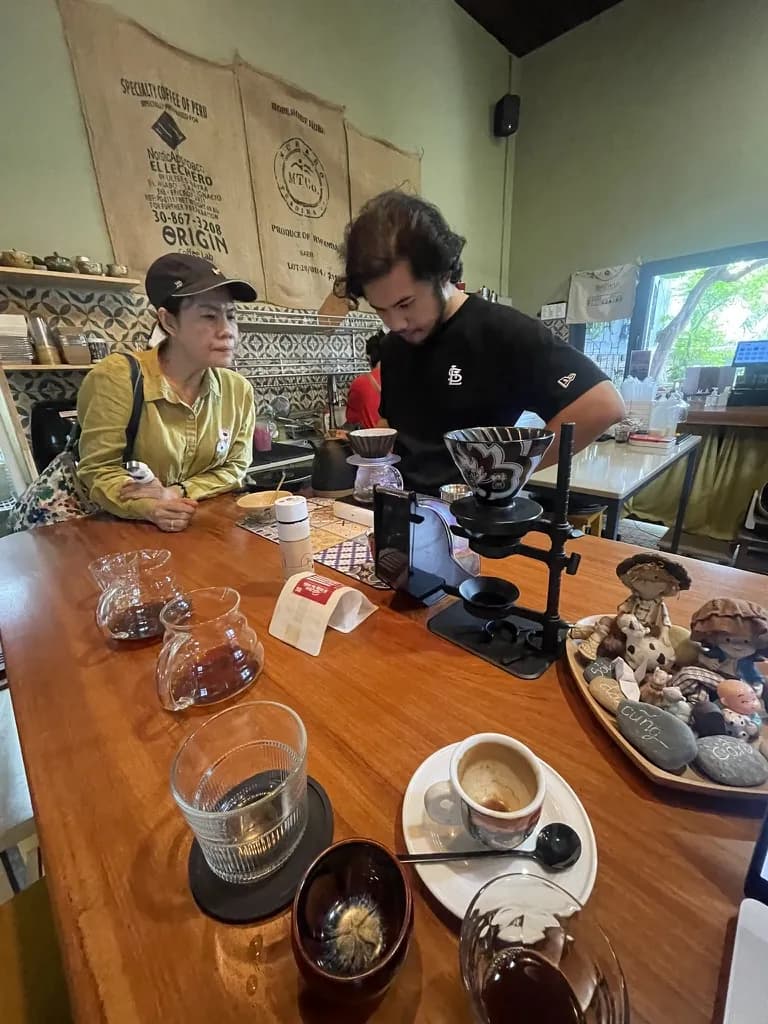 A café owner named Phúc preparing coffee with a guest at the counter.