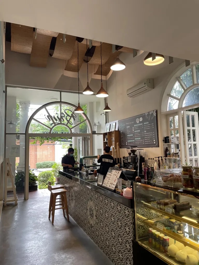 A bright café and bakery with arched windows, espresso equipment, and a pastry case.
