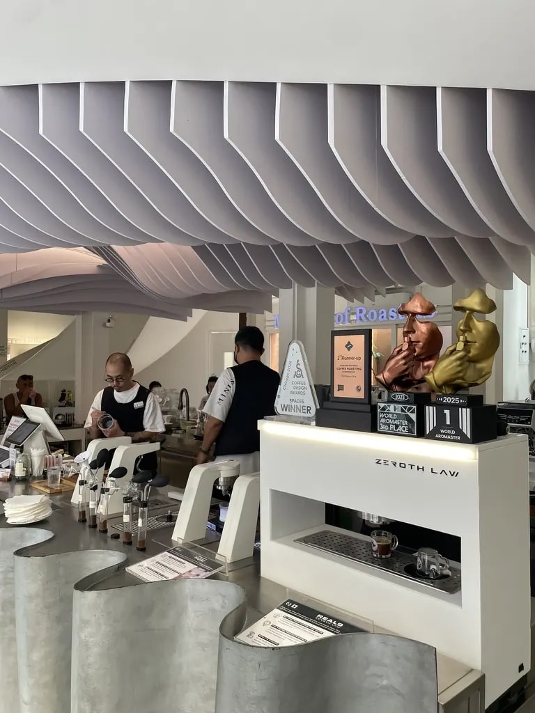 A modern coffee bar with award trophies and a sculptural white espresso machine.