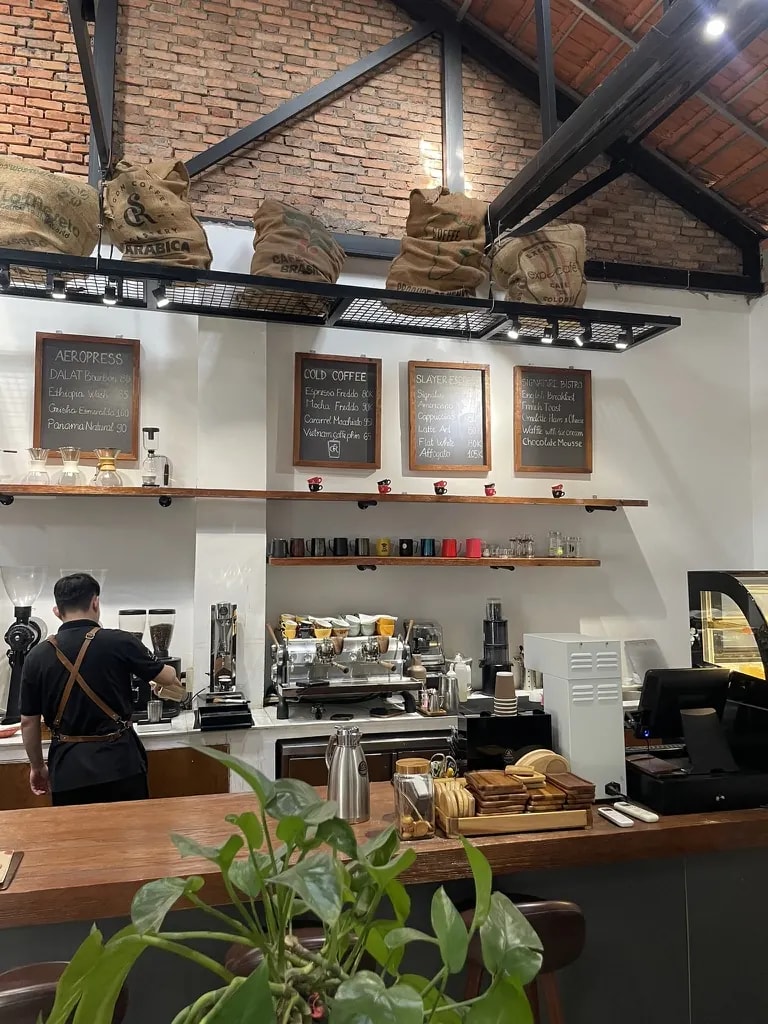 A brick-walled coffee bar with coffee sacks, espresso equipment, and a barista.