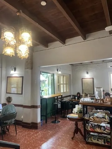 A colonial-style café lounge with chandeliers, books, and small tables.