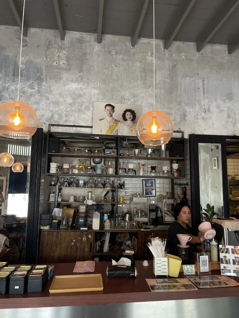 An eclectic concrete café with warm pendant lights, shelves, and a barista.