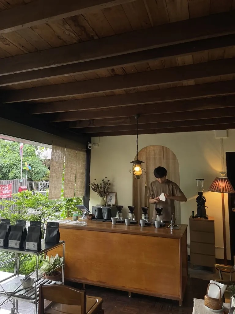A garden-facing café bar with pour-over brewers and a barista preparing coffee.