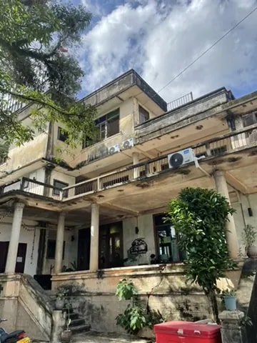 A weathered heritage building surrounded by trees and tropical plants.
