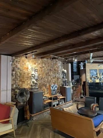 A dark listening-room café with a wood ceiling, speakers, records, and lounge chairs.