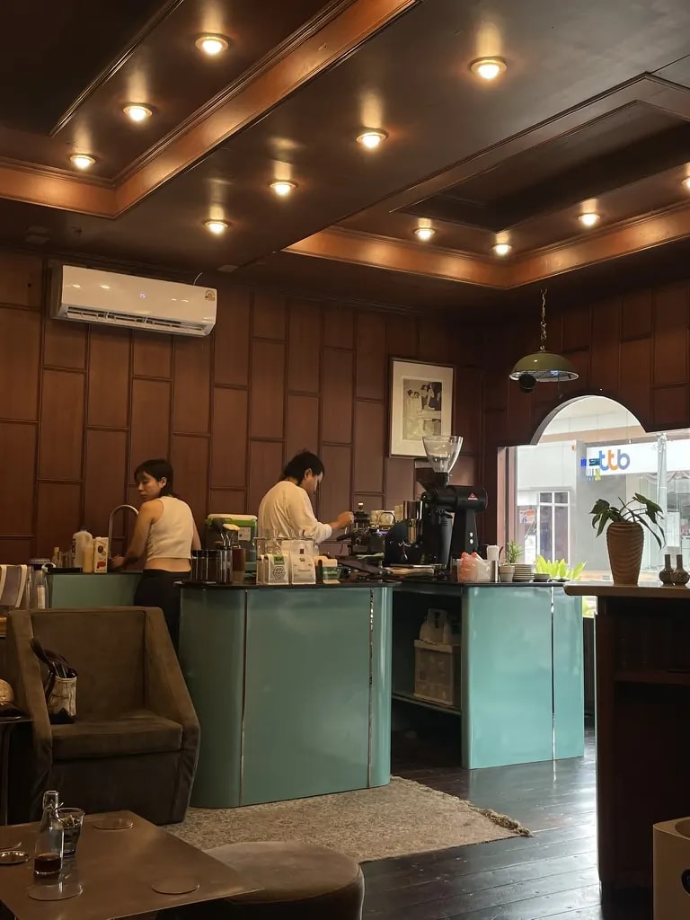 A warm wood-panelled café with a teal service counter and baristas working.