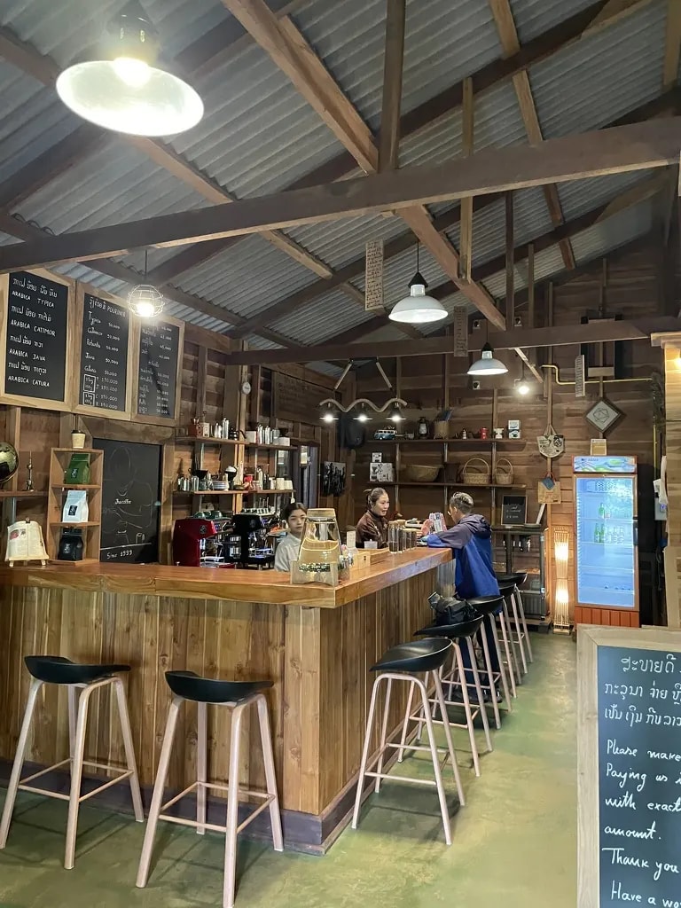 A wooden Laos café with a long bar, tall stools, and handwritten menus.