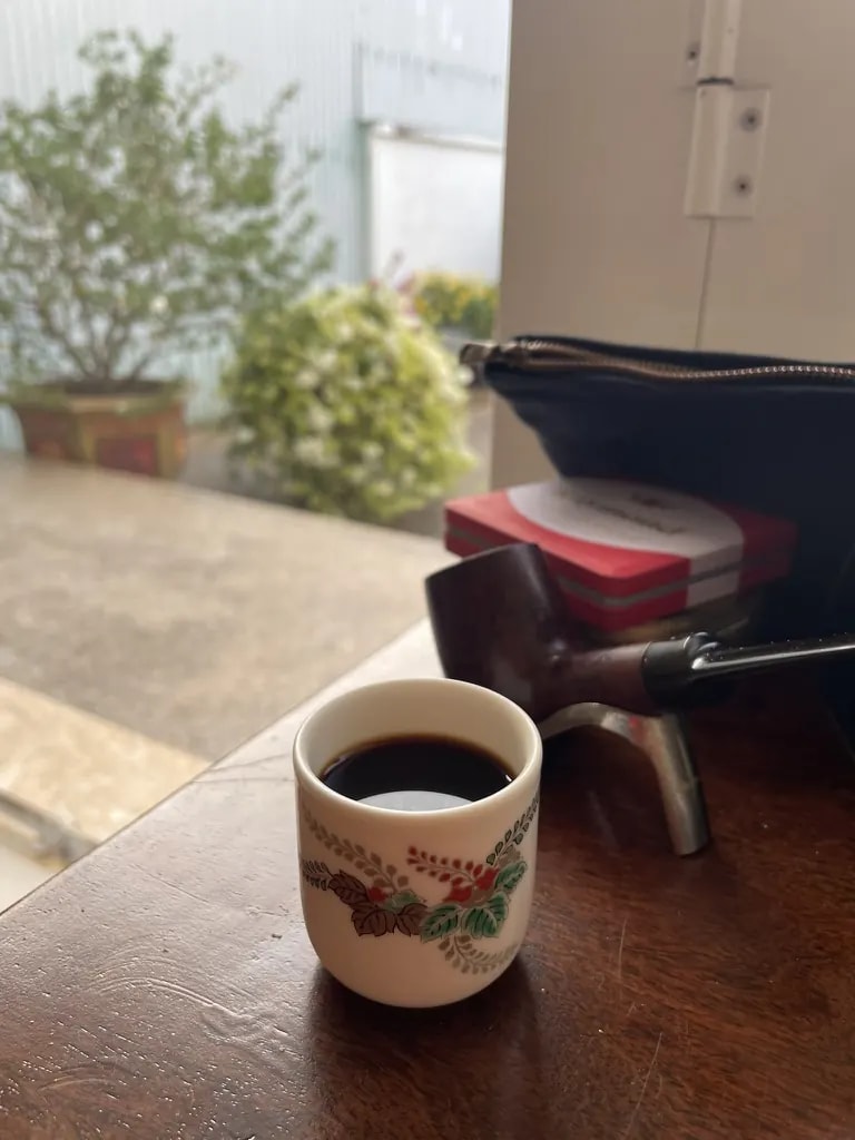 Black coffee in a small floral ceramic cup near a bright window.