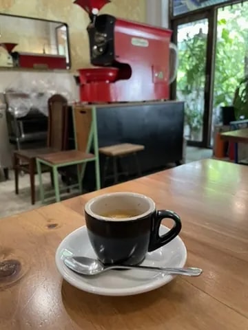 A black espresso cup with a red espresso machine in the background.