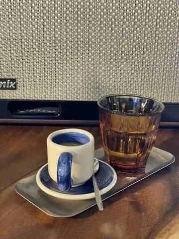 A blue espresso cup and an amber glass of water on a steel tray.