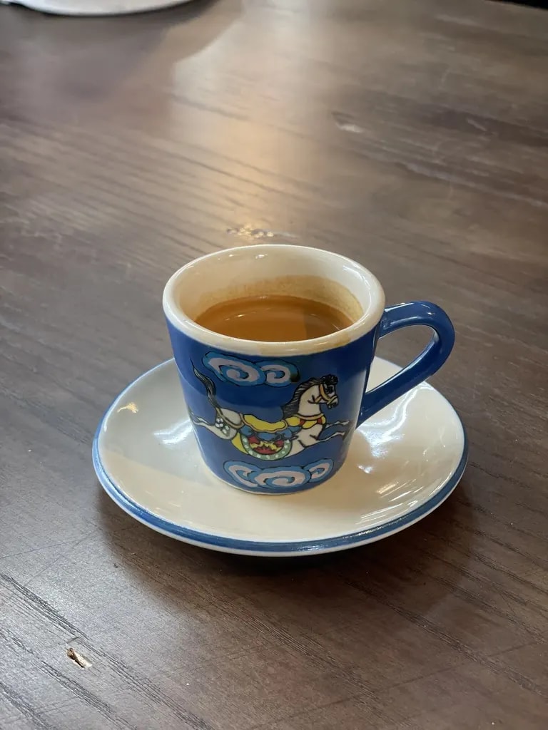 Espresso in a blue illustrated ceramic cup on a white saucer.