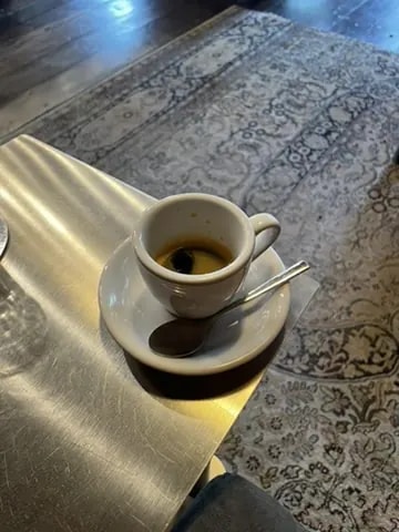 A white espresso cup catching sunlight on the edge of a brass table.