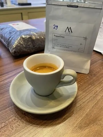 A white espresso cup served beside a bag of coffee beans.