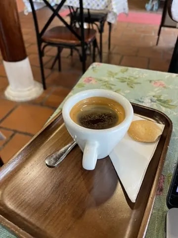 An espresso cup with a small cookie on a wooden tray.