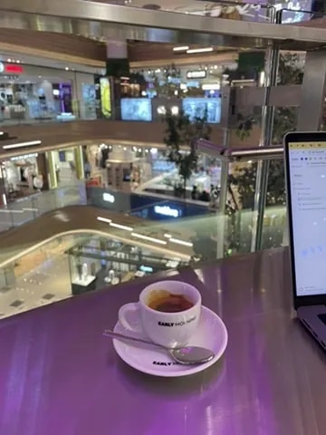 An espresso cup beside a laptop overlooking a shopping centre.