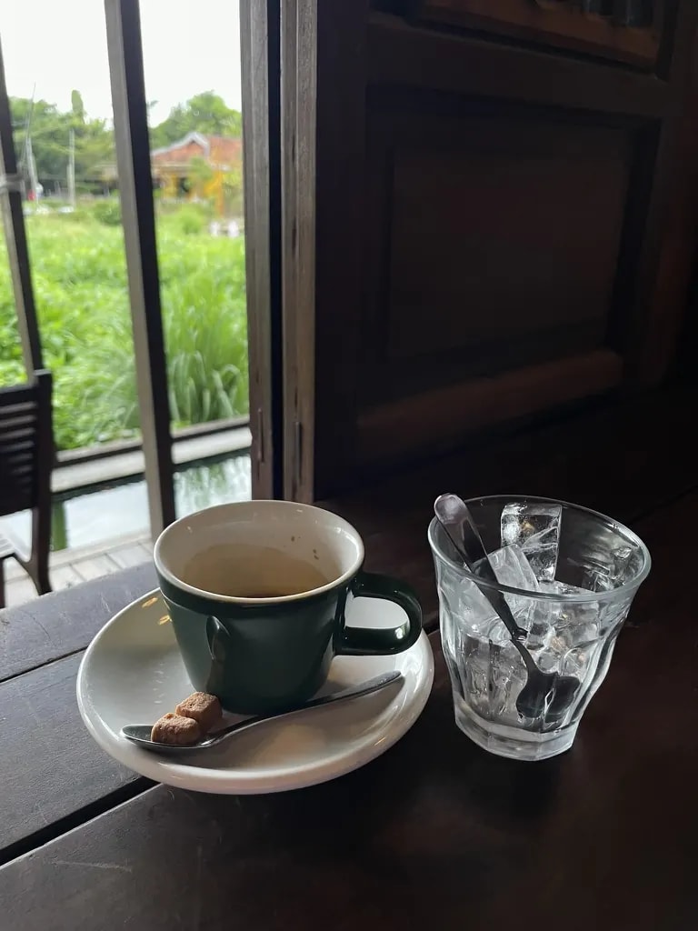A green espresso cup and a glass of ice beside a garden window.