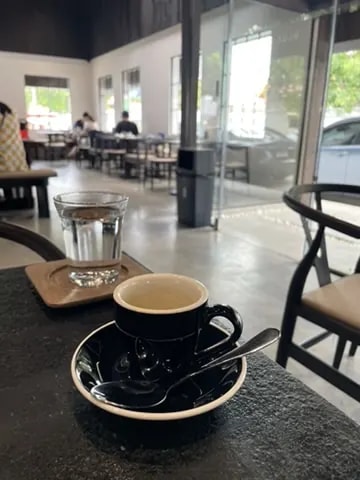 A black espresso cup and water in a bright industrial café.