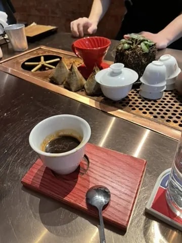 An espresso cup served on a red wooden board beside a tea counter.