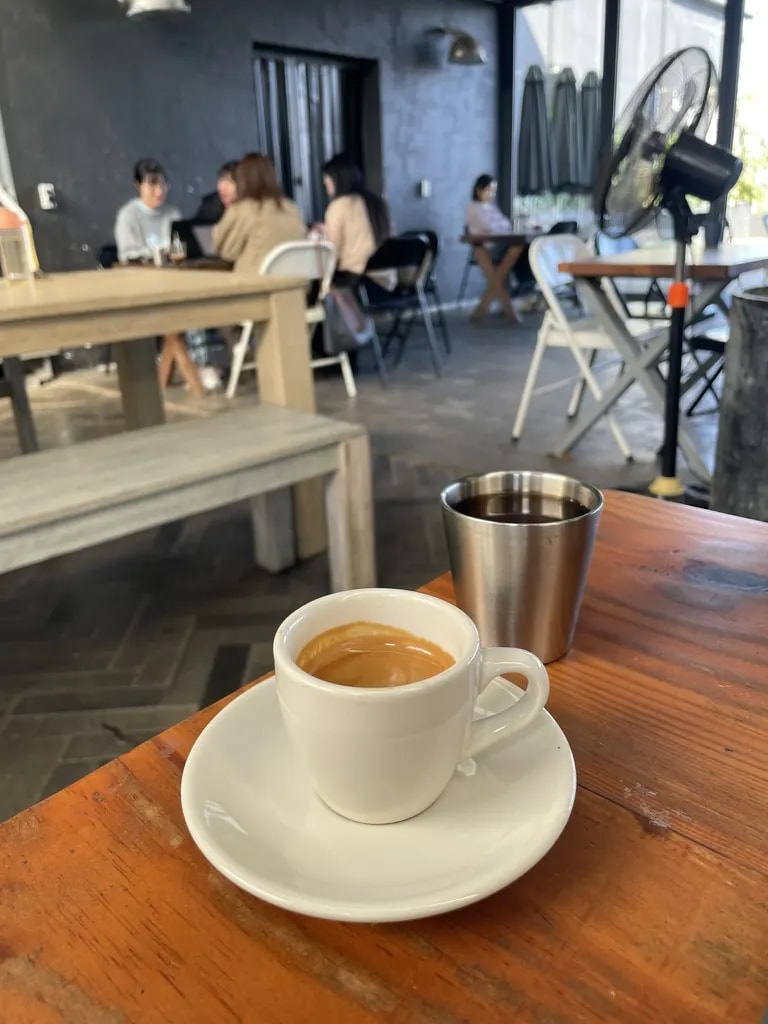A white espresso cup and a steel water cup on a café table.