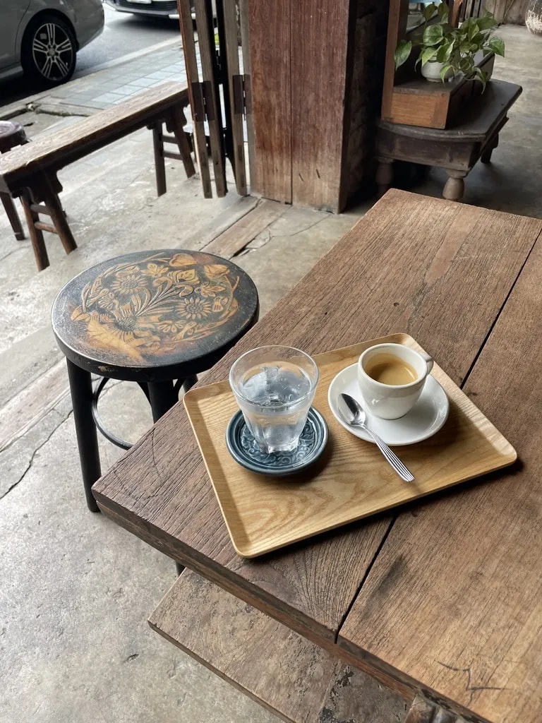 Espresso and water served on a wooden tray beside an old café stool.