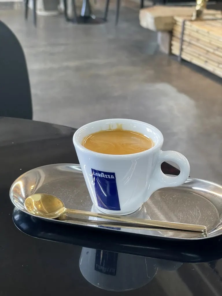 A Lavazza espresso cup with a gold spoon on a steel tray.