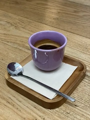 Espresso in a purple ceramic cup on a small wooden tray.