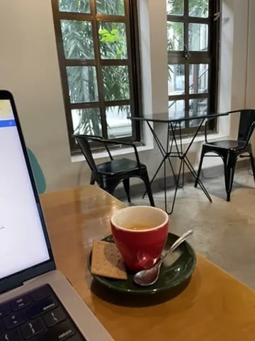 A red espresso cup beside a laptop in a windowed café.