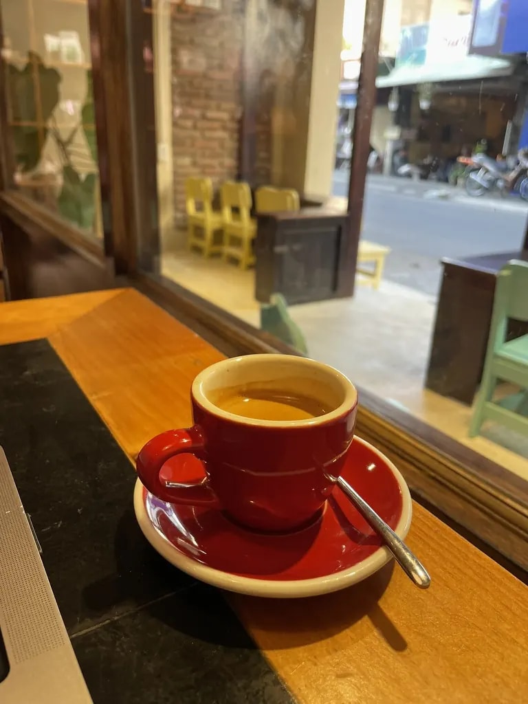 Espresso in a red cup beside an open café window.